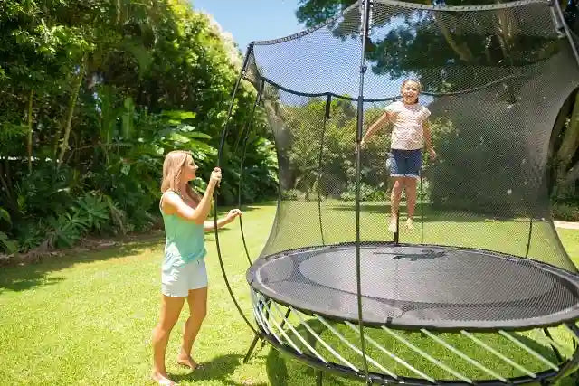 girl jumping on a trampoline while her mother is watching her