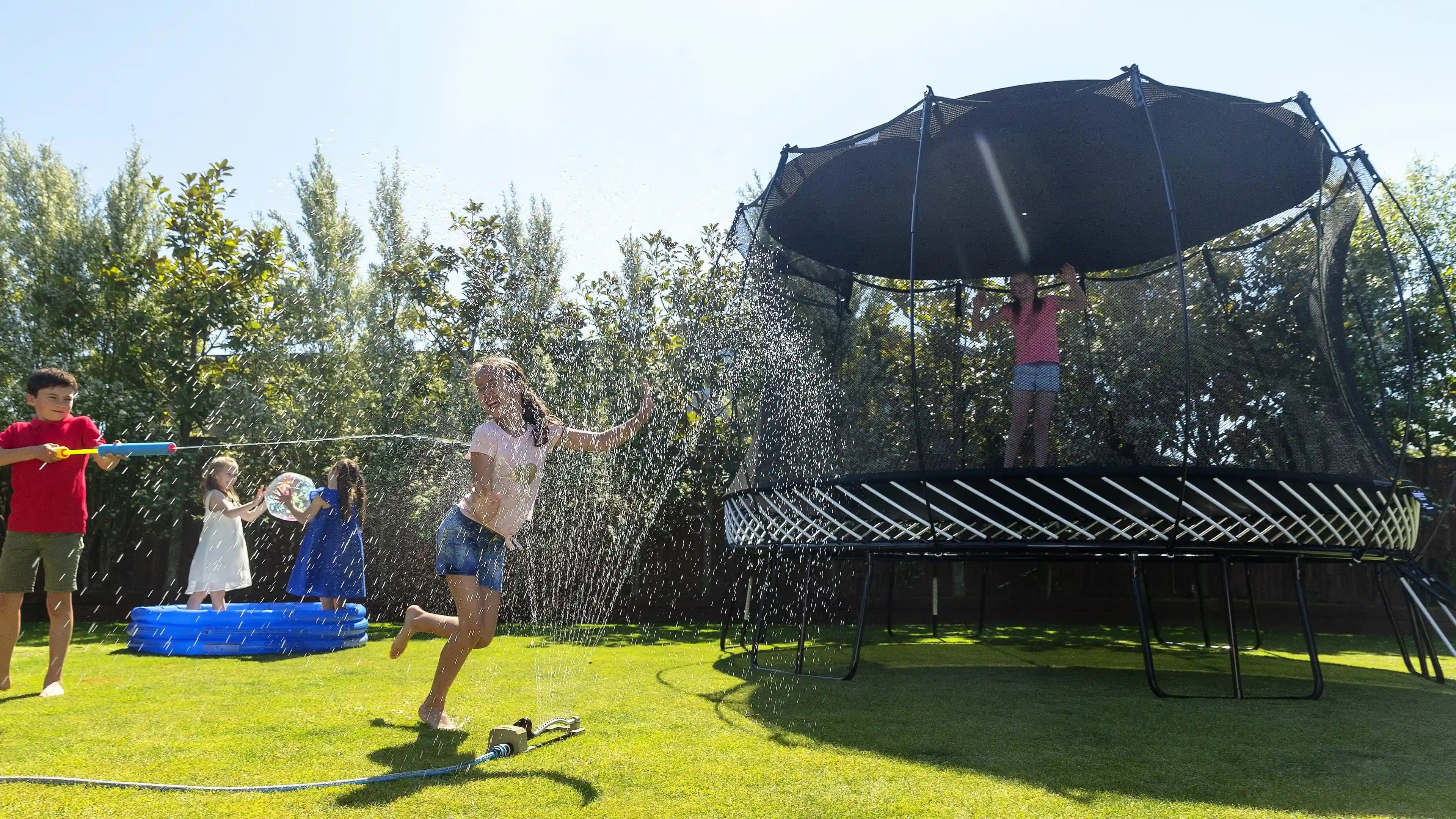 kids playing around a trampoline with a sun shade